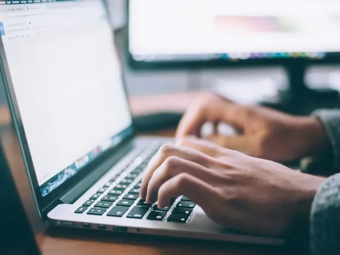 Hands typing on a laptop at a clean workspace with a monitor behind, illustrating research on Local Directory Base